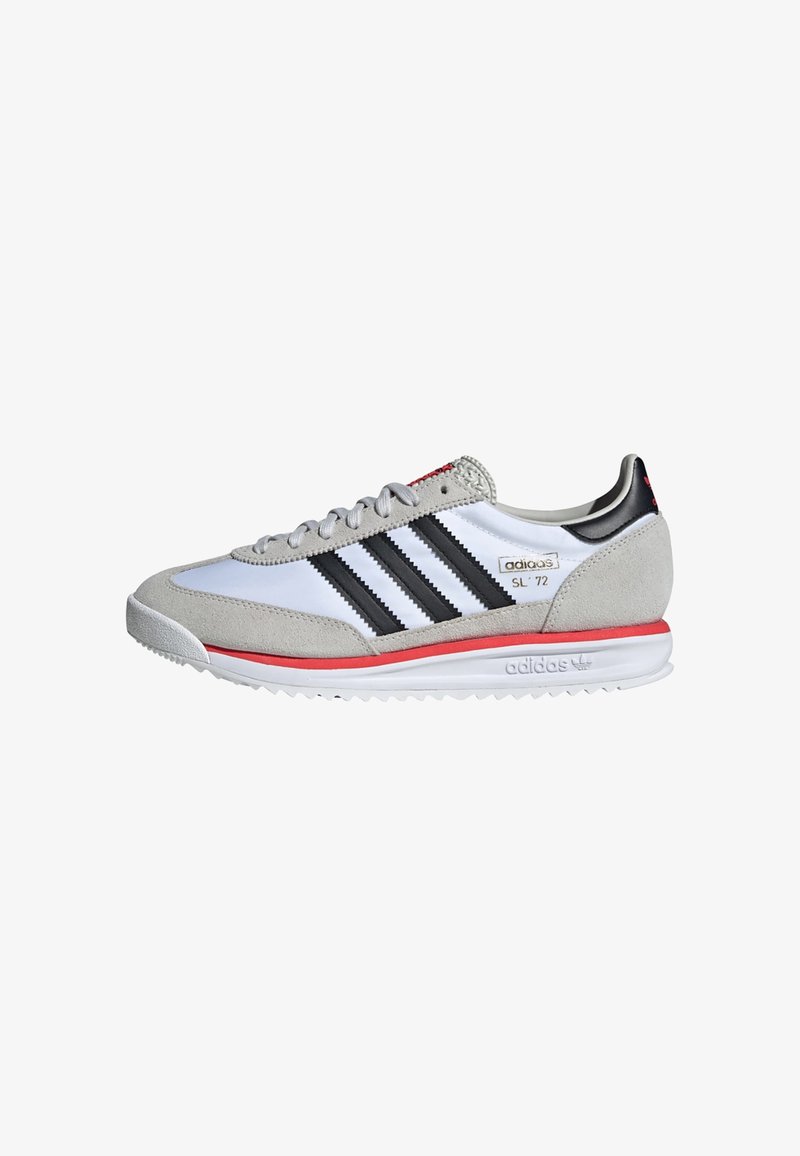 Hvit sneaker med grå semsket skinn detaljer, svarte striper, røde detaljer og en teksturert gummisåle. Har polstret krage og lisser.