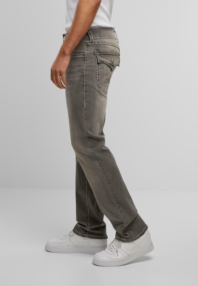Jean en denim gris avec une coupe droite, dotés de coutures contrastées et de poches arrières. Associés à des baskets blanches.