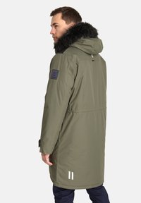 Alkano žalias parka su pūkine kapucho, vandeniui atsparus audinys, reguliuojama talija ir šoninis pleistras ant rankovės. Yra balti akcentiniai raštai.