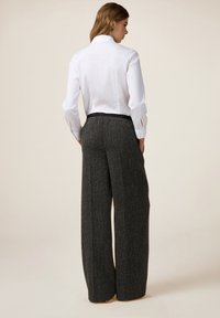 Witte shirt met een kraag aan de achterkant en lange mouwen, gecombineerd met donkergrijze wijde pijpen broek van een gestructureerde stof met elastische tailleband.