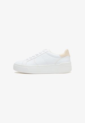 Witte lage sneaker met beige hielstuk, vetersluiting en dikke zool, zijaanzicht op een witte achtergrond.