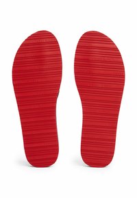 Insoles di scarpe in gomma rossa con scanalature orizzontali e marchio in rilievo. Punta e tallone arrotondati, progettati per comfort e supporto.