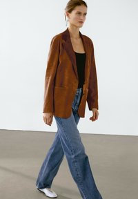 Brun läderblazer med slag, enkel knappstängning, två framfickor, i kombination med ljusblå vida jeans och vita sneakers.