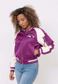 Fioletowa satynowa kurtka bomberka z kremowymi rękawami, zamkami na rękawach, ściągaczami na rękawach oraz haftowanym kwiatowym wzorem na piersi.