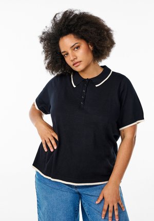 Black polo shirt with short sleeves, white trim at the collar and hem, featuring a button placket and textured fabric detail. Paired with blue jeans.