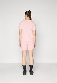 T-shirt en coton rose à manches courtes, arborant un logo "CHAMPION" délavé au dos, associé à un short rose assorti et des chaussettes noires.