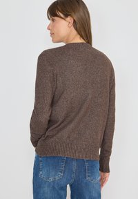 Brun stickad tröja med rund hals, ribbade ärmslut och nederkant, med en strukturerad yta. Bärs med mörkblå jeans.