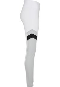 Leggings de sport blancs avec une taille haute, dotées d'un panneau gris et d'accents en chevrons noirs sur les côtés, fabriqués en tissu extensible.