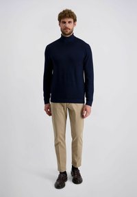 Marineblauwe coltrui van zacht materiaal, gecombineerd met beige broek. Heeft lange mouwen, een getailleerd ontwerp en ribbelmanchetten.