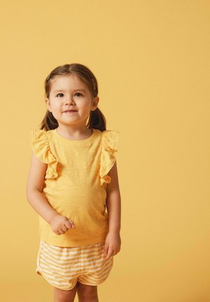 Gelbes Oberteil mit Rüschensleeves und passenden gestreiften Shorts. Leichter Stoff, lässiges Design und einfarbiger gelber Hintergrund erhöhen die Sichtbarkeit.