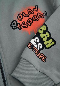 Szary sweatshirt z kolorowymi grafikami: pomarańczowy napis "PLAY SPRAY" i wielokolorowy napis "ESBN". Widoczne ściągacze przy rękawach i zamek.