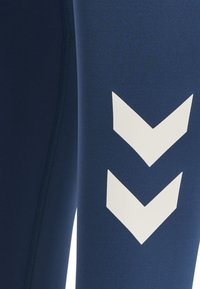 Granatowe legginsy sportowe wykonane z elastycznego materiału, z białymi wzorami w zygzak wzdłuż boku. Zawierają widoczne detale szwów.