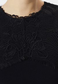 Czarna koronkowa dekolt z kwiatowymi wzorami na ciemnym materiale, zbliżenie na obszar kołnierza i górnej części klatki piersiowej.