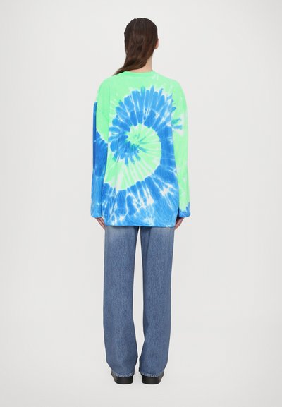 Long-sleeve tie-dye shirt in neon green and blue, features a spiral pattern. Paired with wide-leg denim pants, showing a casual style.