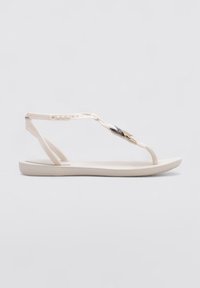 Sandalias planas de color crema con un empeine trenzado, que cuentan con un acento en negro y dorado. Hechas de un material flexible con una suela plana.