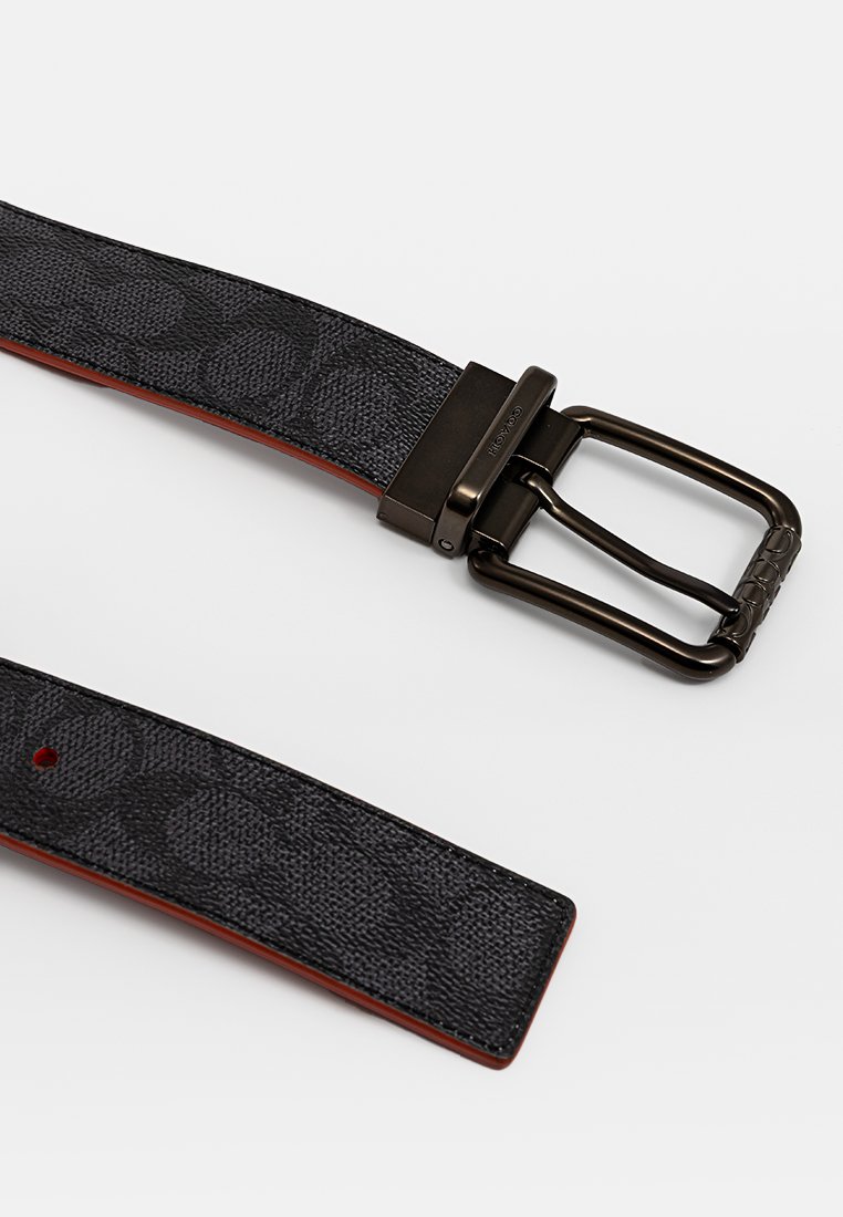 Schwarzer Stoffgürtel mit geprägtem Muster, Lederunterlage und einer Metallschnalle in dunkler Ausführung. Die Nähte sind entlang der Kanten sichtbar.