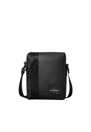 Bolso bandolera cuadrado negro con correa ajustable, parche con el logo de Calvin Klein y sutil tira vertical de marca en el lado izquierdo delantero.