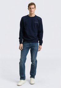 Marineblauwe katoenen sweatshirt met ronde hals, geribbelde manchetten en zoom. Gecombineerd met lichtblauwe spijkerbroek en beige sneakers. Eenvoudige logodetail op de borst.