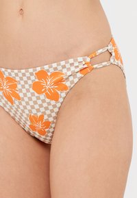 Bas de bikini à carreaux avec des motifs de fleurs orange, fabriqué en tissu doux, doté de découpes latérales et d'un design ajusté.