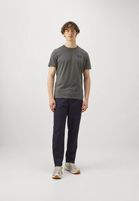 Pelēka īsroku t-krekls ar logo uz krūtīm, kombinēts ar tumši ziliem biksēm un bēšām kedām ar oranžām detaļām. Gluda auduma tekstūra.