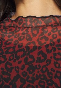 Genomskinlig topp i ett djärvt röd- och svart leopardmönster. Rundad halslinning med scallop-kant. Lätt och strukturerad material.