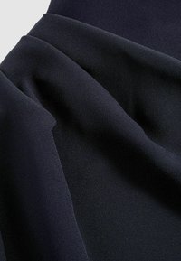 Měkká, tmavá látka elegantně splývá, předvádí hladké záhyby a texturu v hluboké námořnické modři, čímž zdůrazňuje svůj luxusní vzhled.
