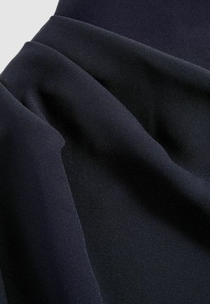Mäkká, tmavá látka elegantne splýva a vystavuje hladké záhyby a textúru v hlbokej námorníckej modrej, zdôrazňujúc jej luxusný vzhľad.