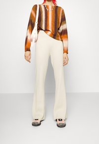 Pull en maille à rayures horizontales marron, orange et crème ; pantalon évasé côtelé crème ; sac à main rose ; baskets colorées.