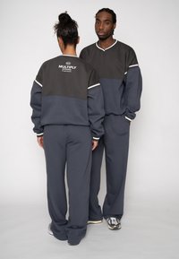 Gray matching sweatshirt and pants set, featuring a contrasting dark gray upper, ribbed cuffs, and logo on the back. Soft fabric with relaxed fit.