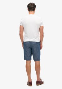 Męska biała koszulka T-shirt zestawiona z niebieskimi szortami dżinsowymi, charakteryzująca się prostym wzorem, teksturowanym materiałem i dwiema tylnymi kieszeniami z guzikami.