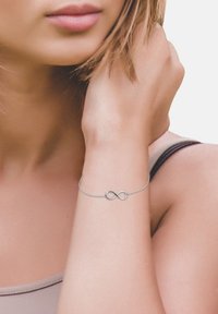 Bracciale in argento con simbolo dell'infinito, dal design delicato e dalla texture liscia, indossato su un polso con una carnagione chiara.