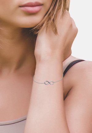 Bracciale in argento con simbolo dell'infinito, dal design delicato e dalla texture liscia, indossato su un polso con una carnagione chiara.