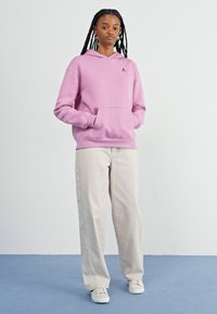 Pink hooded sweatshirt with a front pocket and ribbed cuffs, paired with light beige wide-leg pants and white sneakers.