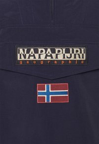 Marineblå pullover med frontlynlås, der har "NAPAPIJRI" logo patch og broderet norsk flag. Tekstureret stof med kontrasterende syninger.