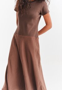 Brązowa prążkowana sukienka dzianinowa z krótkim rękawem na górze i luźno opadającą spódnicą, lekko ciemniejsza na dole, o swobodnym kroju.