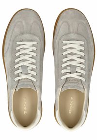 Zapatillas de ante gris claro con cordones y detalles blancos, que cuentan con un interior beige y una suela de goma texturizada. La marca es visible en el costado.