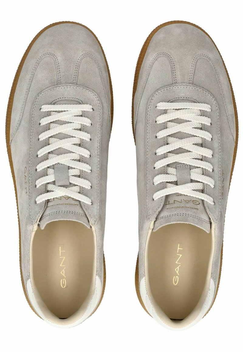 Jasnoszare zamszowe sneakersy z białymi sznurówkami i akcentami, z beżowym wnętrzem i teksturowaną gumową podeszwą. Widoczne logo po bokach.