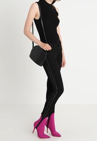 Svart ribbad ärmlös topp med hög halsdesign, tillsammans med högmidjade svarta jeans med sidostripes. Rosa stilettstövlar med dragkedjor.