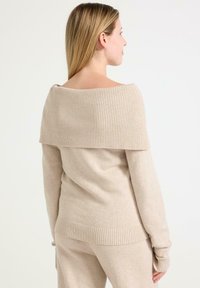 Beżowy sweter dzianinowy z szerokim prążkowanym dekoltem typu off-the-shoulder, długimi rękawami oraz prążkowanymi detalami u dołu. Miękka, teksturowana tkanina.
