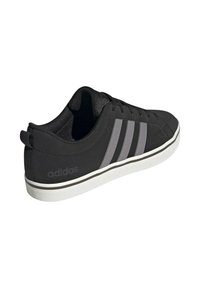 Zapato deportivo negro con parte superior lisa, con tres rayas grises, suela de goma blanca y forro de tela texturizada.