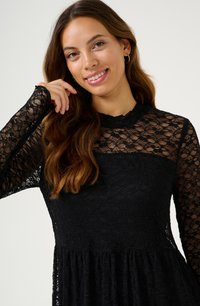 Rochie neagră din dantelă cu mâneci lungi, guler înalt și un corset texturat, având o fustă evazată. Model floral detaliat pe întreaga suprafață.