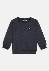 Mørkegrå hettegenser med lange ermer, rund hals og ribbestrikkede mansjetter; har en liten rund svart brodert logo på brystet.