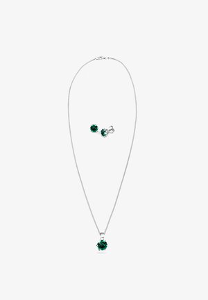 Silberne Halskette mit einem einzelnen grünen Edelstein-Anhänger und passenden grünen Ohrsteckern, die ein elegantes Design und eine polierte Oberfläche zeigen.