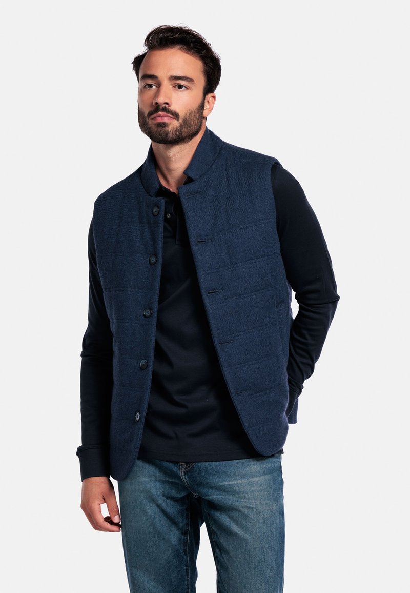 Marine blauwe verzepte vest gemaakt van gestructureerde stof, met een staande kraag, knopen aan de voorkant en zijzakken, gedragen over een donker shirt.