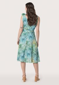 Robe d'été florale dans des teintes vertes et bleues, présentant un corsage ajusté, une jupe fluide et des nœuds aux épaules, confectionnée en tissu léger.