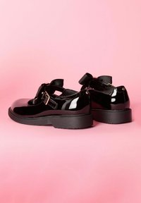Pantofi Mary Jane din piele lacuită neagră, cu vârf rotunjit, curea la glezna și accent cu fundiță, având o talpă din cauciuc texturat negru.