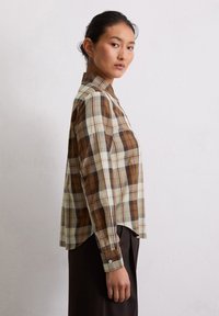 Chemise à carreaux brun et crème avec un col, des manches longues et un ourlet légèrement arrondi, fabriquée en tissu léger en mélange de coton.