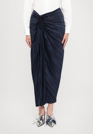 Navy pleated skirt with twisted detail at the waist. Features a smooth texture and ankle length, paired with metallic silver shoes.