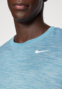 Lyseblå treningsskjorte med glatt tekstur, rund hals og en hvit Nike-logo på venstre skulder.