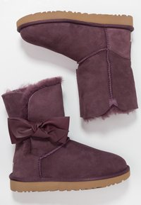 Paire de bottines en daim violet avec semelles en caoutchouc marron clair, dotées d'une doublure duveteuse et d'un nœud décoratif en cuir sur le côté externe.